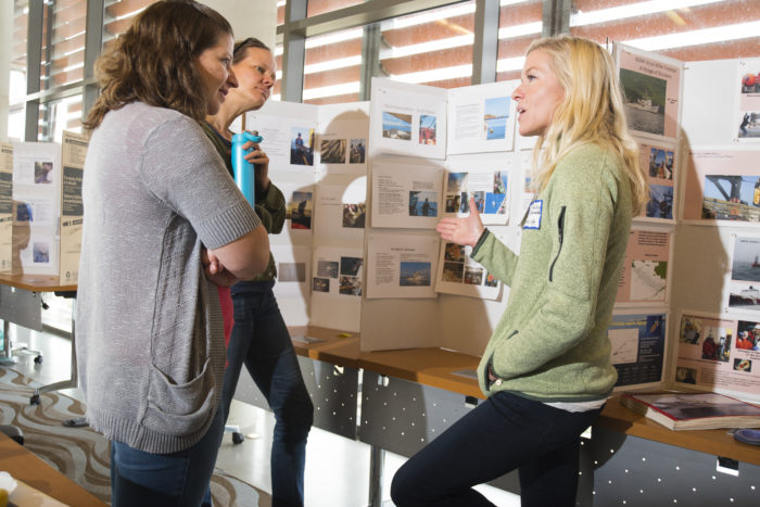 Three adult women standing in front of poster board presentations and having a conversation.