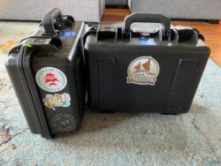 Two black cases, covered with stickers, sitting on the ground.