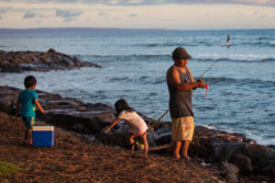 a fisherman and two young children stand on the shore with fishing gear