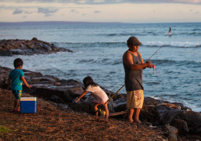 a fisherman and two young children stand on the shore with fishing gear