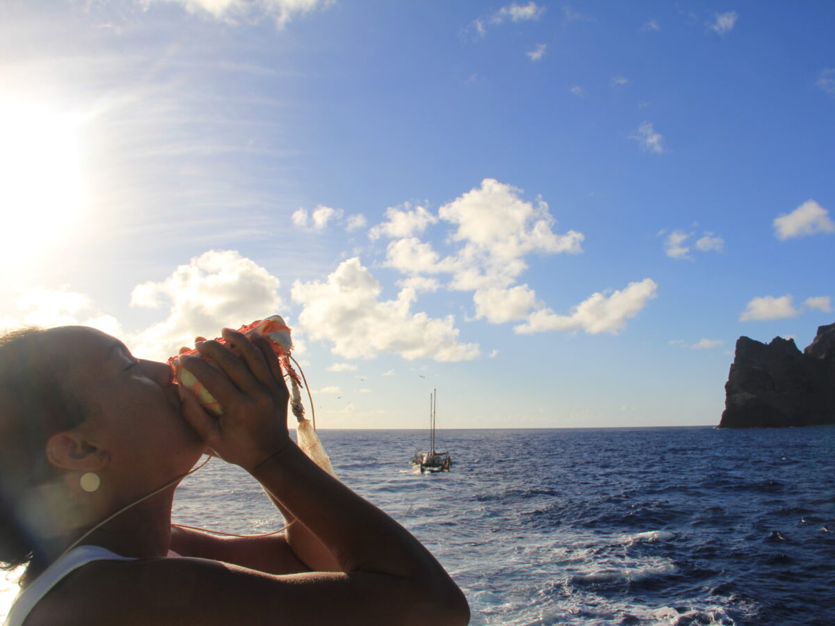 Native Hawaiian sounds a conch in the presence of Nihoa and Hōkūleʻa.