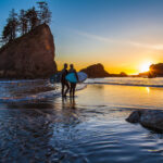 Two surfers holding boards standing at the shoreline at sunset